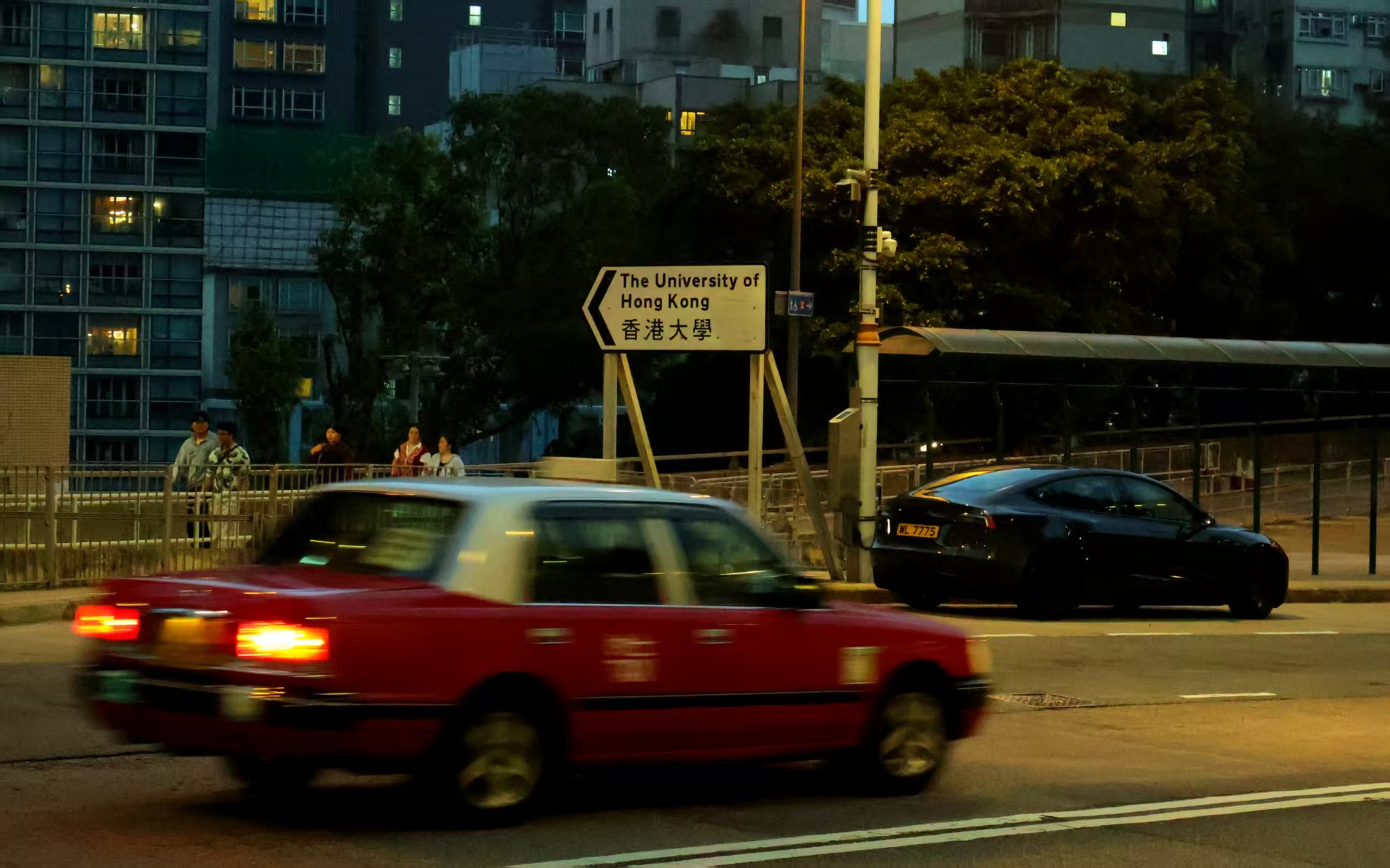 A red taxi passing through a tree-lined Hong Kong street