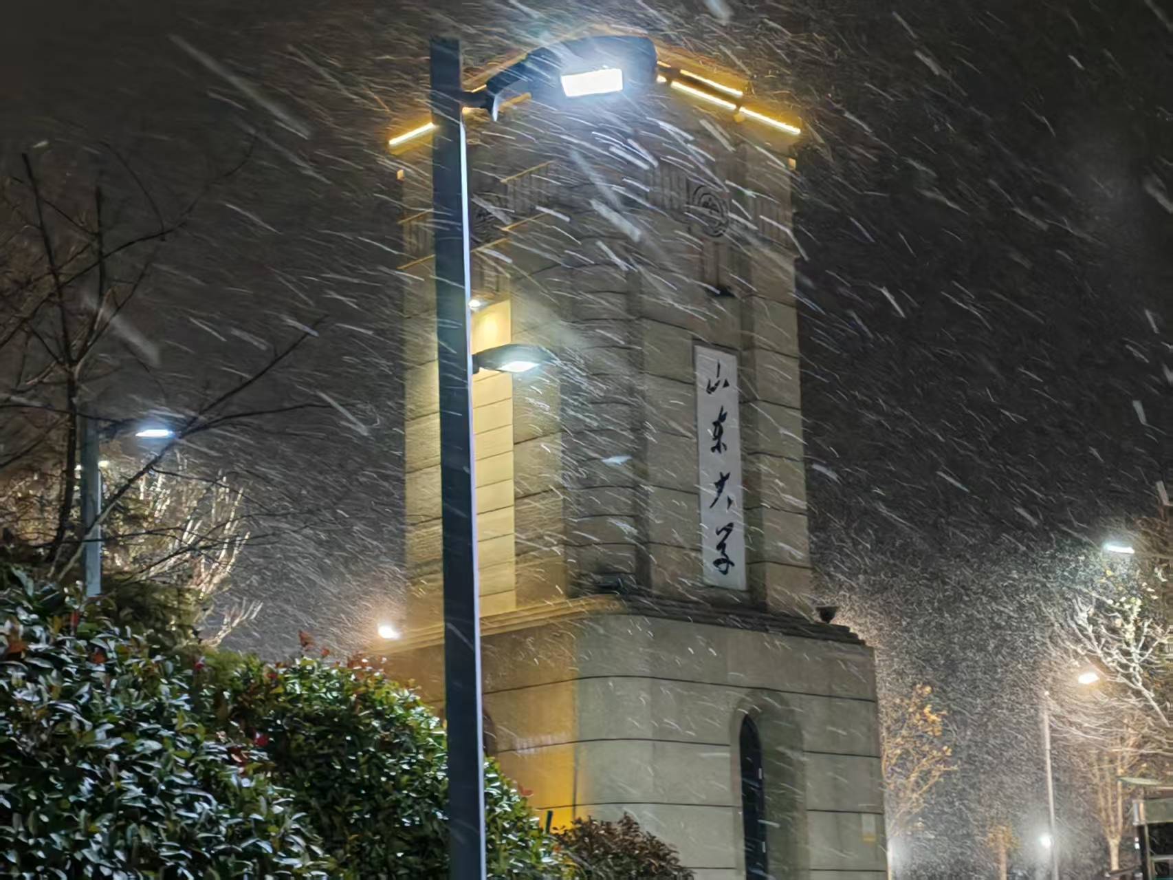 Snow falling around a lit campus monument in Qingdao