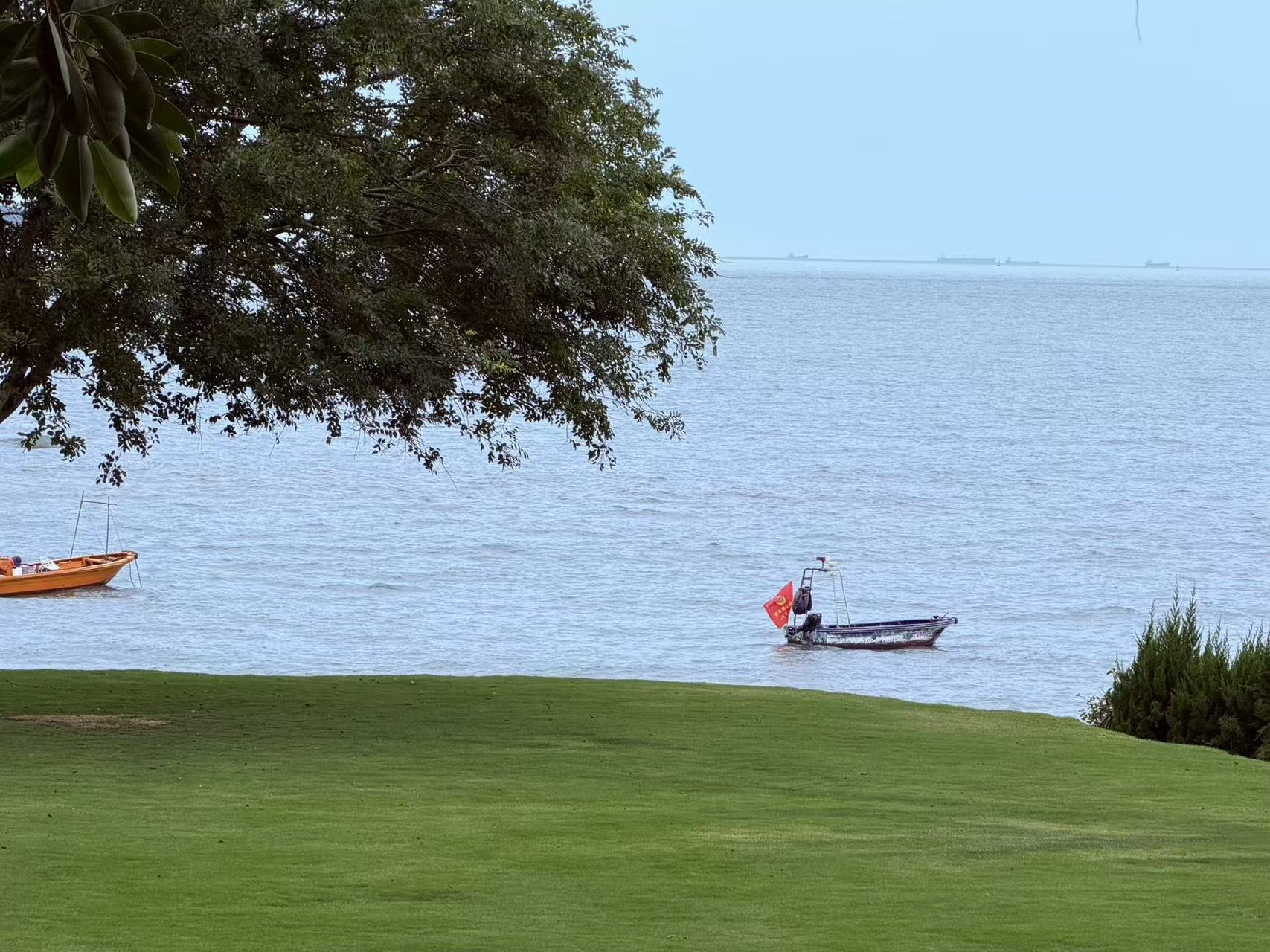A small boat beyond a green coastal lawn in Xiamen